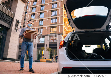 Low-angle shot of delivery man wearing medical protective mask holding carton boxes with hot pizza. 71359259