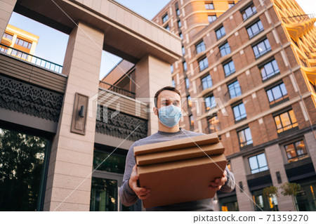 Low-angle shot of delivery man wearing medical protective mask holding carton boxes with hot pizza. 71359270