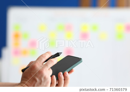 In his hands he holds a smartphone and stylus for electronic signature In his hands he holds a smartphone and stylus for electronic signature 71360379
