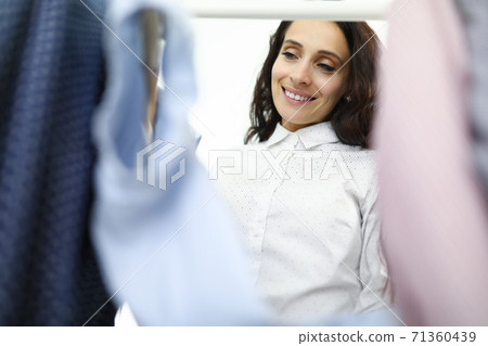 Smiling woman inspects clothes in wardrobe closeup Smiling woman inspects clothes in wardrobe closeup 71360439