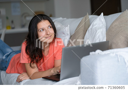 Girl lying on the couch rejoices looking at the laptop. Smiles, good mood, emotion of joy Girl lying on the couch rejoices looking at the laptop. Smiles, good mood, emotion of joy 71360605