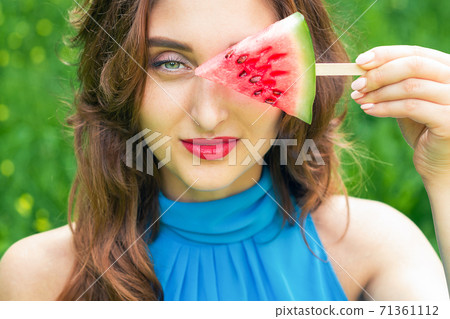 Woman covers eye with watermelon. 71361112