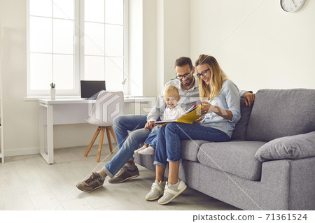 Happy parents and kid sitting on sofa, reading book of stories or looking through family photo album 71361524