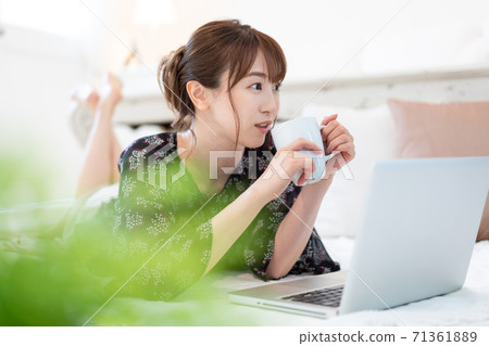 Young woman lying down in the living room, drinking a drink and talking with a zoom 71361889