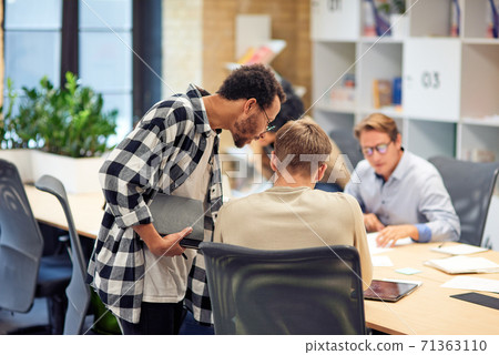Rear view of two young diverse colleagues discussing something while working together in the modern office or coworking space Rear view of two young diverse colleagues discussing something while working together in the modern office or coworking space 71363110
