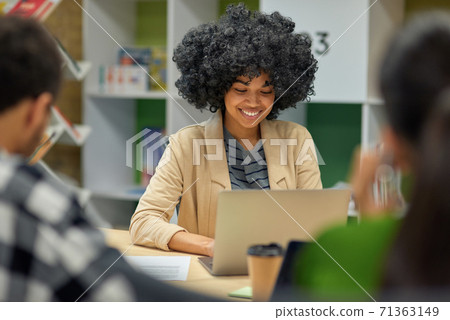 Young cheerful mixed race woman working on laptop in the modern office, selective focus Young cheerful mixed race woman working on laptop in the modern office, selective focus 71363149