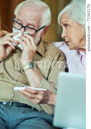 Sick elderly man checking temperature while his wife supporting him Sick elderly man checking temperature while his wife supporting him 71363179