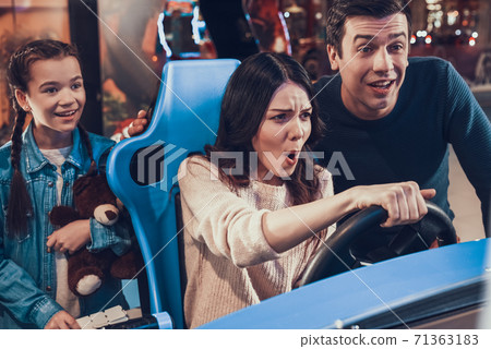 Mom drives toy car in game while daughter watches. 71363183