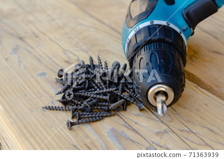 A pile of black wood screws and a drill close-up. 71363939