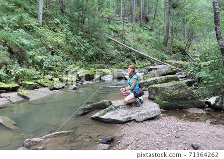 Happy woman sitting on a stone by the river Happy woman sitting on a stone by the river 71364262