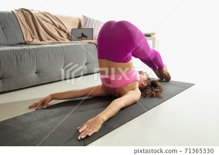 Beautiful young woman working out indoors, doing yoga exercise on gray mat at home Beautiful young woman working out indoors, doing yoga exercise on gray mat at home 71365330