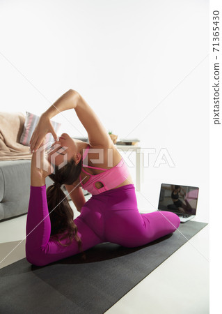 Beautiful young woman working out indoors, doing yoga exercise on gray mat at home Beautiful young woman working out indoors, doing yoga exercise on gray mat at home 71365430
