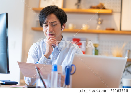 Telework Young man thinking while looking at web conference documents in his living room 71365716