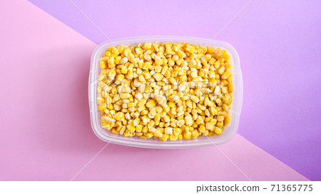 Corn in a plastic container for long-term storage. Deep freezing of vegetables. Frozen food vegetables on color background. Corn in a plastic container for long-term storage. Deep freezing of vegetables. Frozen food vegetables on color background. 71365775