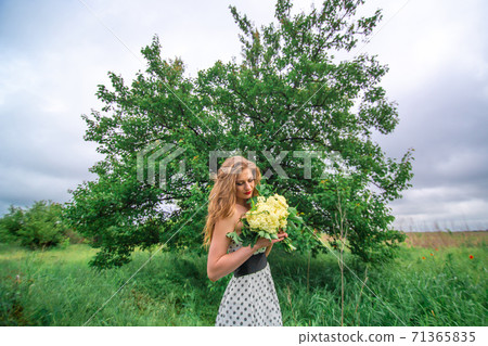 A beautiful young blonde girl collected a bouquet of wildflowers. Enjoy a walk on a warm summer day 71365835
