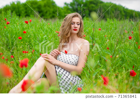 A young long-haired girl enjoys the colors of nature on a blooming poppy field on a hot summer day 71365841