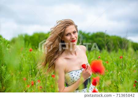 A young long-haired girl enjoys the colors of nature on a blooming poppy field on a hot summer day A young long-haired girl enjoys the colors of nature on a blooming poppy field on a hot summer day 71365842