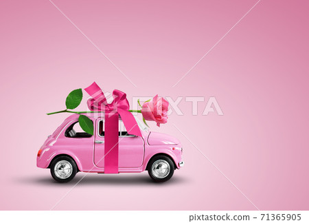 Pink toy car delivering pink rose flower on pink background. Flowers delivery, women day, valentine day. 71365905