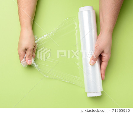 two female hands hold a roll of transparent cling film for packaging products two female hands hold a roll of transparent cling film for packaging products 71365950