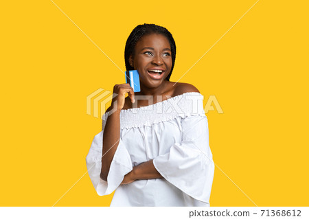Positive black lady dreaming about shopping with credit card in hands Positive black lady dreaming about shopping with credit card in hands 71368612