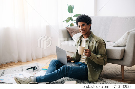 Positive black college student with cup of coffee and laptop listening to online lecture at home, space for text 71368935