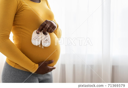 Closeup of baby shoes on pregnant black lady belly 71369379
