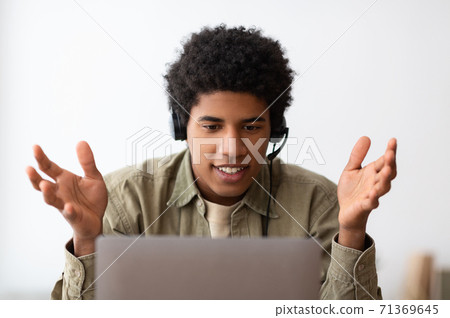 Web based education concept. Happy black teen student in headset talking to his college tutor online on laptop, indoors Web based education concept. Happy black teen student in headset talking to his college tutor online on laptop, indoors 71369645
