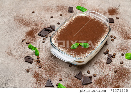 Traditional Italian Tiramisu dessert in glass baking dish on concrete background Traditional Italian Tiramisu dessert in glass baking dish on concrete background 71371336