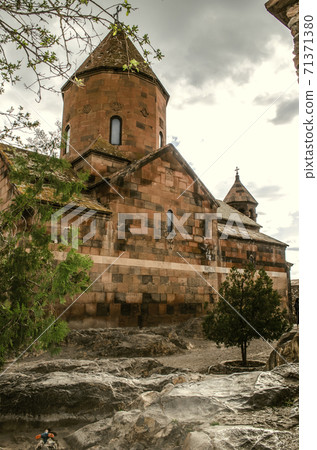 The reverse side of the medieval Church of the blessed Holy Virgin with a bell tower among trees and basalt boulders in the spring rain 71371380