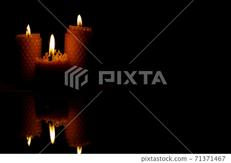 Close-up of three small yellow candles on a black background. Close-up of three small yellow candles on a black background. 71371467