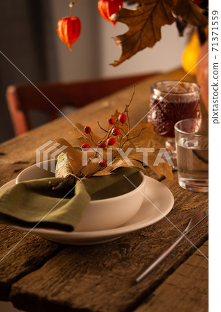 Green napkin with dry oak leaf and rosehip branch on a plate 71371559