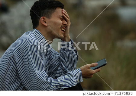 A man holding a smartphone and distorting his face 71375923