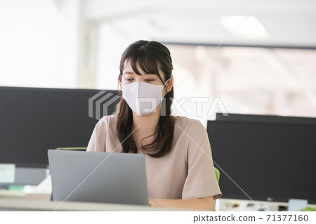 A woman wearing a mask and doing desk work in the office 71377160
