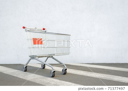 Empty Grocery Cart on the White Wall Store. Trolley at the Supermarket Background. E-commerce. Shopping Concept. Side View. Shopping Cart Trolley Stands near Mall with Copy Space. Black Friday Sale 71377497