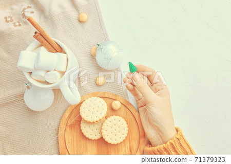 Women holds Christmas toy, cup of coffee, cookies and tablecloth on table. Women holds Christmas toy, cup of coffee, cookies and tablecloth on table. 71379323