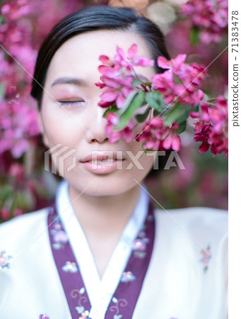 Portrait of Asian girl with her eyes closed, standing in front of a branch of cherry blossom that cover her face. The concept of a pleasant oriental aroma, the freshness of the oriental garden Portrait of Asian girl with her eyes closed, standing in front of a branch of cherry blossom that cover her face. The concept of a pleasant oriental aroma, the freshness of the oriental garden 71383478