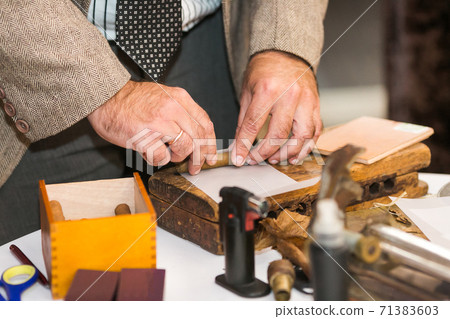 Men's hands roll up a cigar of high quality raw materials using vintage wooden cigar making tools Men's hands roll up a cigar of high quality raw materials using vintage wooden cigar making tools 71383603