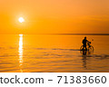 Silhouette of a person who rolls his bike next to him walking the shallow water, leisurely strolling along the shoreline in the sunset. The concept of rest from city life and active rhythm. 71383660