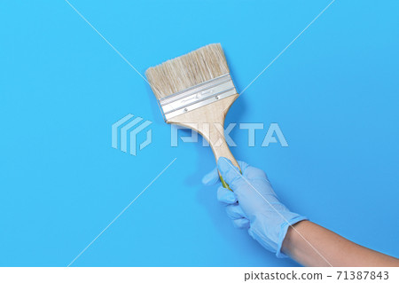 Brush for paint in hand on a blue background. Brush for paint in hand on a blue background. 71387843