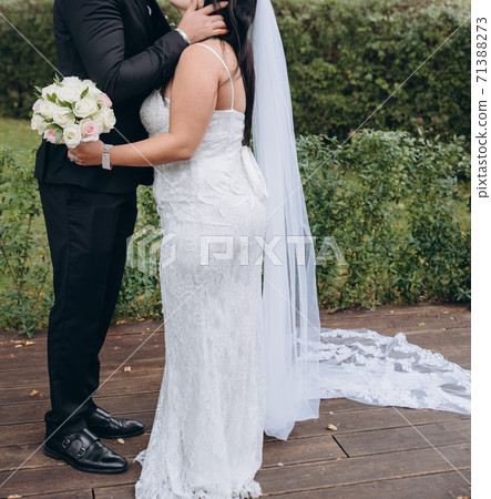 Bridal couple kissing, young bride wears white dress and holds wedding bouquet of roses. 71388273