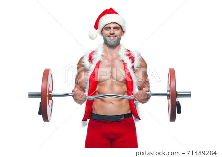 Sexy Santa Claus. Bodybuilder young handsome santa clause smile in red santa hat train muscles arms and biceps at New Years eve and Christmas winter holiday white background. Sexy Santa Claus. Bodybuilder young handsome santa clause smile in red santa hat train muscles arms and biceps at New Years eve and Christmas winter holiday white background. 71389284