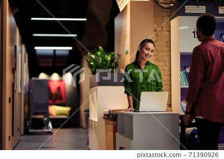 Young cheerful asian woman talking with colleague while standing together in corridor of the modern office Young cheerful asian woman talking with colleague while standing together in corridor of the modern office 71390926