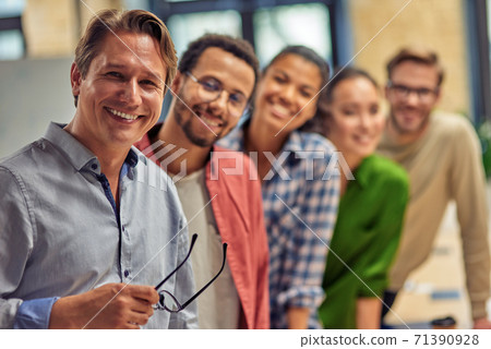 Powerful team. Group of young happy multiethnic colleagues smiling at camera while standing in the modern office, business people working together Powerful team. Group of young happy multiethnic colleagues smiling at camera while standing in the modern office, business people working together 71390928