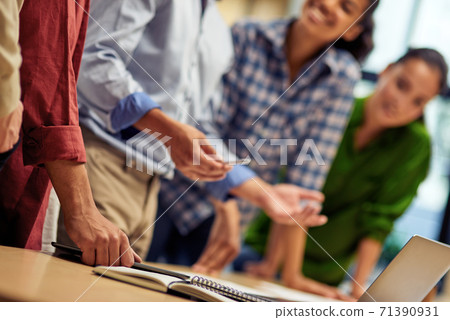 Businessman explaining something to young multiracial colleagues while working together in the office, using laptop Businessman explaining something to young multiracial colleagues while working together in the office, using laptop 71390931