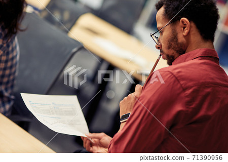 Young mixed race man analyzing document while working in the modern office, selective focus Young mixed race man analyzing document while working in the modern office, selective focus 71390956