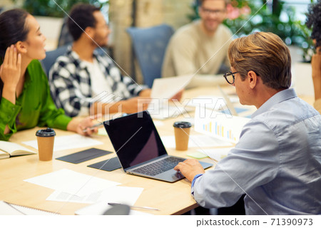 Teamwork. Group of young multiracial people sitting at the table in board room in the modern office, using modern technologies and working on project together Teamwork. Group of young multiracial people sitting at the table in board room in the modern office, using modern technologies and working on project together 71390973