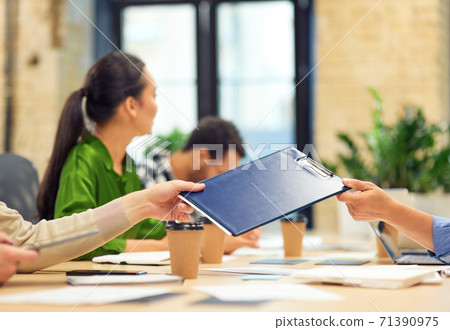 Male coworker giving a folder with documents to his colleague while working in the modern office Male coworker giving a folder with documents to his colleague while working in the modern office 71390975