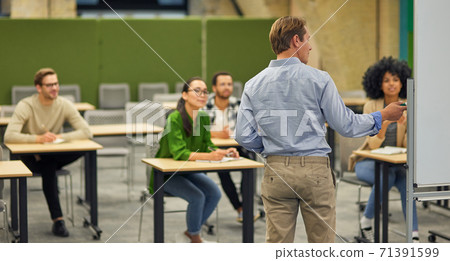 Rear view of a male business coach or speaker pointing at flip chart and giving presentation to audience, Rear view of a male business coach or speaker pointing at flip chart and giving presentation to audience, 71391599