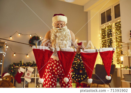 Old Santa Claus hanging his red caps to dry after doing laundry on winter holidays Old Santa Claus hanging his red caps to dry after doing laundry on winter holidays 71391902