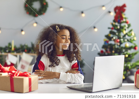 Happy African American girl using laptop for video call or watching a Christmas movie Happy African American girl using laptop for video call or watching a Christmas movie 71391918